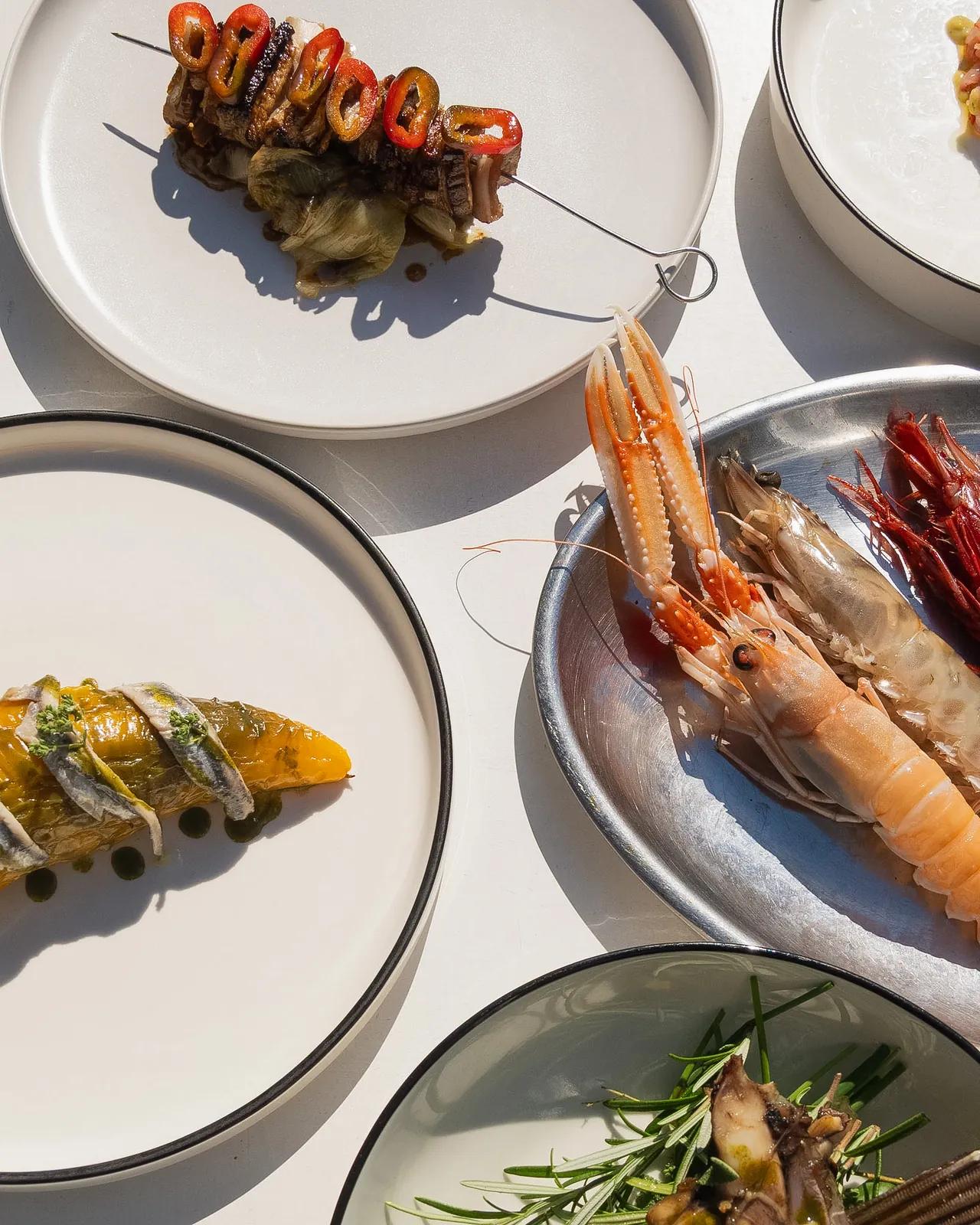 Selezione di antipasti di mare in tavola: spiedino, crostacei crudi e peperone con alici